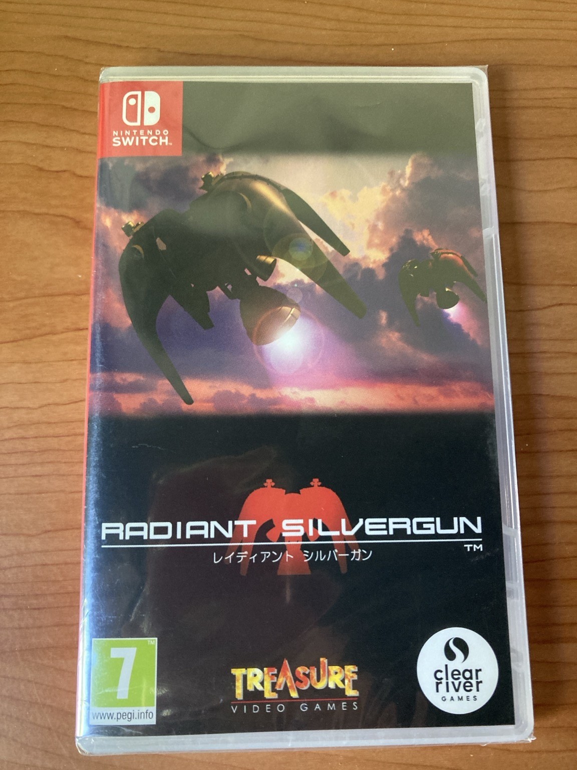 A Nintendo Switch game case for "Radiant Silvergun," featuring futuristic aircraft against a cloudy background. The cover includes the game's title in English and Japanese, along with logos for the developer, Treasure, and the publisher, Clear River Games.