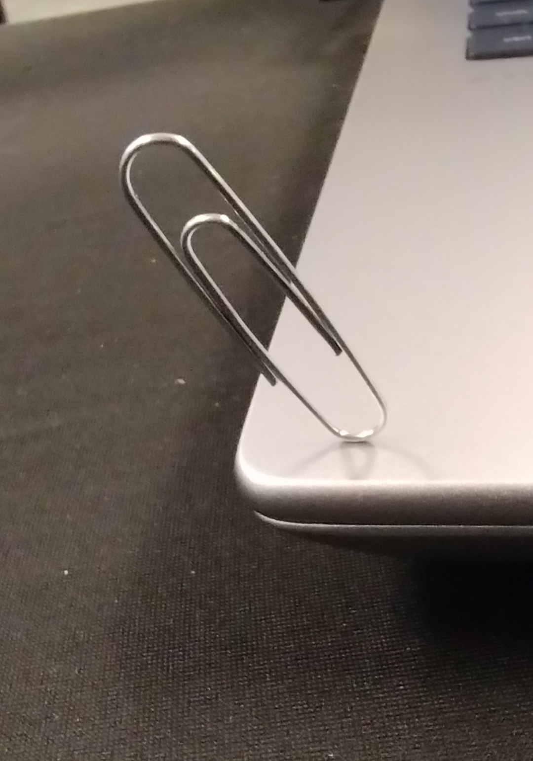 photo of a paperclip standing on its edge at a 30 degree angle on top of a laptop